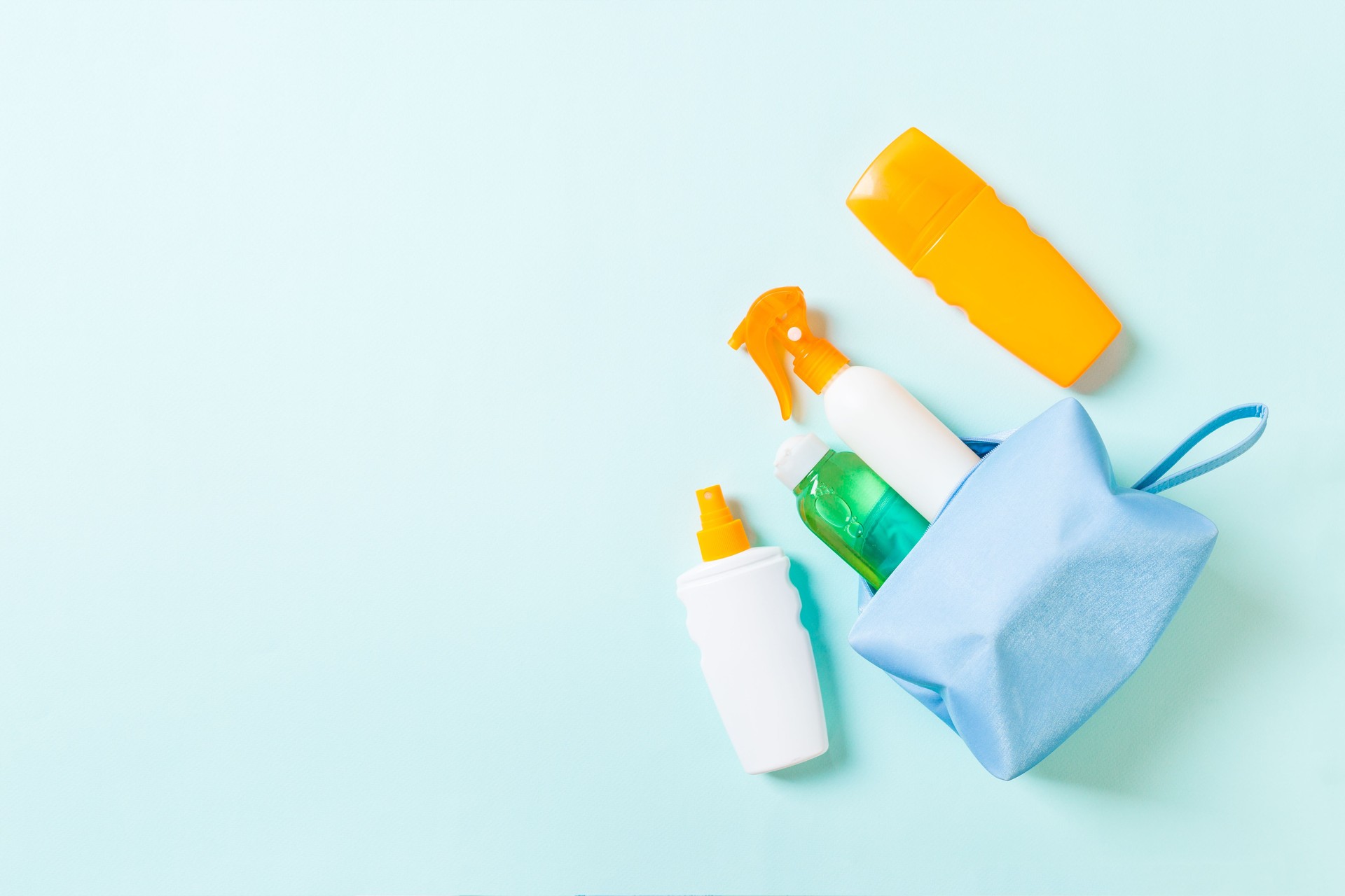 Top view of female cosmetics bag full of suncream spray, sunsreen, sunblock and body lotion and spf cream on blue background with copy space. Directly above. Bright summer concept